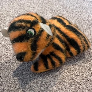 May include: A plush tiger toy with orange and black stripes. The toy has a white patch on its chest and green eyes.