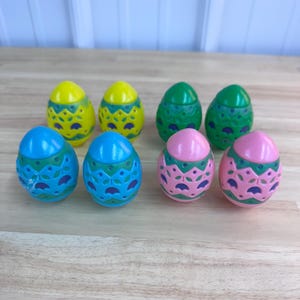 May include: A collection of eight colorful plastic Easter eggs. The eggs are yellow, green, blue, and pink, each with a decorative floral design. The eggs are arranged on a wooden surface.