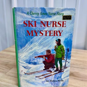 May include: Vintage book titled "Ski Nurse Mystery" by Helen Wells. The cover features a snowy mountain scene with two people on skis. The book has a blue cover with red and green text.