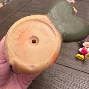 May include: Vintage rubber Mickey Mouse toy with a green hat and red shoes. The bottom of the toy has a circular base with the text "Walt Disney Made in Japan" printed on it.