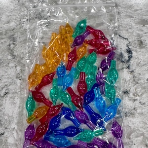 May include: A clear plastic resealable bag filled with a collection of small, translucent, flame-shaped decorative light covers in various colors including yellow, red, purple, blue, and green, designed for use with string light sets.