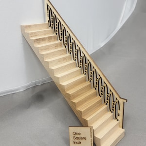Puede incluir: Una escalera de madera en miniatura con una barandilla decorativa. Las escaleras son de color claro, con una barandilla calada marrón oscuro. Un pequeño cuadrado de madera con el texto "One Square Inch" está en la base. Las escaleras son un artículo de artesanía o casa de muñecas.
