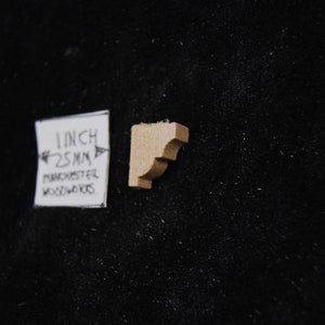 May include: A small, unfinished wooden corbel, measuring 1 inch or 25 mm. The corbel is a decorative architectural element used to support a shelf or other structure.
