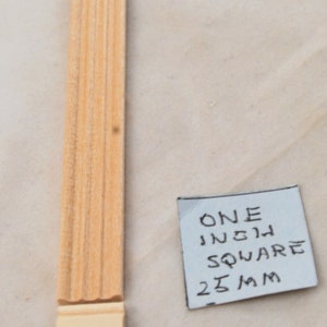 Op de afbeelding: Een close-up van een houten lijststrip, ongeveer een inch vierkant, of 25 mm. De lijst heeft een decoratief, geribbeld ontwerp.