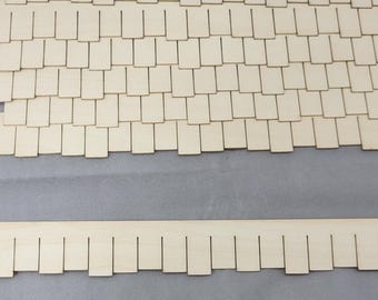 Op de afbeelding: Houten miniatuur dakspanen en sierstukken. De dakspanen zijn rechthoekig en in een verspringend patroon gerangschikt. Een klein vierkant stuk is gemarkeerd met "One Square Inch". Het sierstuk heeft een geschulpte rand.