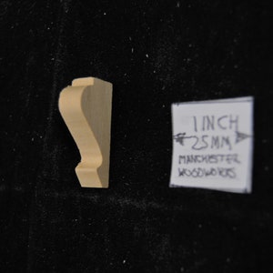 May include: A small, unfinished wooden corbel, measuring 1 inch (2.5 cm) in length. The corbel is a decorative architectural element used to support a shelf or other structure.