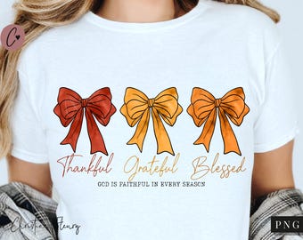 以下が含まれることがあります： 赤、オレンジ、黄色の3色のリボンが描かれた白いTシャツ。「Thankful, Grateful, Blessed」の文字がリボンの下に書かれており、その下に「GOD IS FAITHFUL IN EVERY SEASON」というフレーズが書かれています。