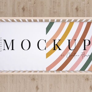 May include: A white crib sheet with a colorful abstract pattern of curved lines in shades of pink, orange, yellow, and green. The sheet has the text "MOCKUP" in black and the text "BY Christine Henry" in cursive.