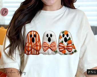 Pode incluir: Camiseta creme com três desenhos de fantasmas bordados. Os fantasmas têm padrões listrados laranja e branco, florais e xadrez, com laços e detalhes pretos de olhos e boca. Uma peça de roupa com tema de Halloween.