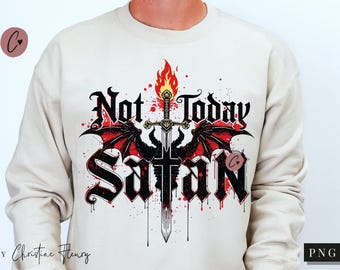 Puede incluir: Sudadera color crema con un diseño gráfico que presenta el texto "Not Today Satan" en una fuente gótica. El diseño incluye una espada, llamas y alas de murciélago rojas. La sudadera es de estilo casual.