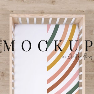 May include: A white crib with a fitted sheet featuring a colorful rainbow pattern in shades of pink, orange, brown, yellow, and green. The text "MOCKUP BY Christine Henry" is visible on the sheet.