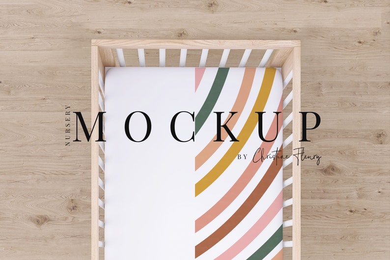 May include: A white cot with a fitted sheet featuring a colourful rainbow pattern in shades of pink, orange, brown, yellow, and green. The text "MOCKUP BY Christine Henry" is visible on the sheet.