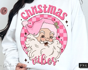 May include: White sweatshirt with a pink and white checkered circle design. The circle features a cartoon Santa Claus with a pink hat and the text "Christmas vibes".