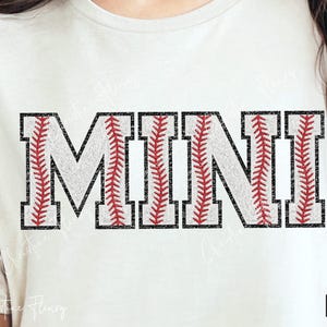 Puede incluir: Camiseta blanca con la palabra "MINI" en un diseño de béisbol. Las letras son blancas con costuras rojas y contornos negros, que simulan pelotas de béisbol. La camiseta la lleva una persona.