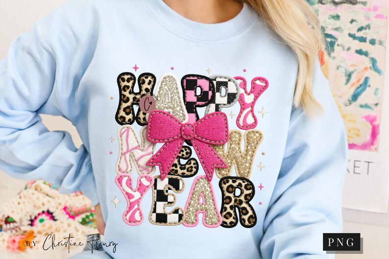 Pode incluir: Camisola azul clara com um design colorido "HAPPY NEW YEAR". O design apresenta um la&ccedil;o rosa, estampa de leopardo e padr&otilde;es xadrez. As letras est&atilde;o em v&aacute;rios estilos e cores, criando um visual festivo.