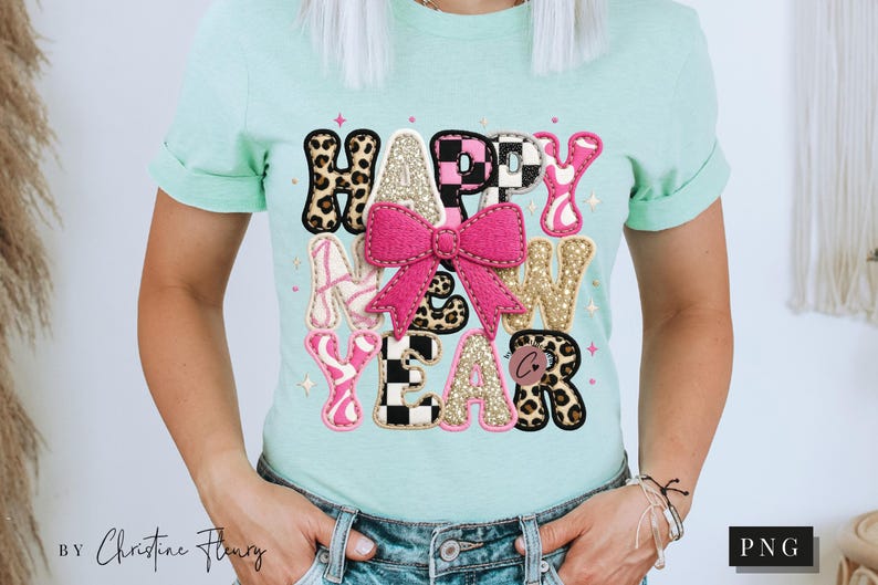 Pode incluir: Uma camiseta verde clara com um design colorido "HAPPY NEW YEAR". O design inclui um la&ccedil;o rosa, letras com estampa de leopardo e detalhes brilhantes. A camiseta &eacute; usada com jeans azuis.