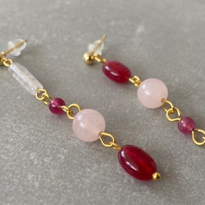 May include: Gold earrings with pink and red gemstone beads. The earrings are made with a chain and have a simple design.