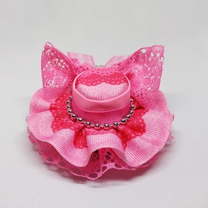 May include: A pink and white hat with a ruffled trim and a silver beaded band. The hat is made of fabric and has a lace trim.