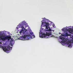 May include: Two purple sequined hair bows with silver glitter centers.