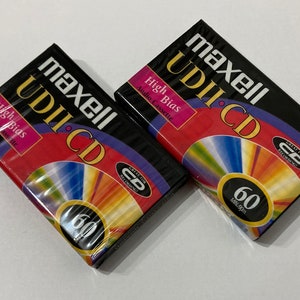 Op de afbeelding: Twee Maxell UDII-CD audiocassettes, elk met een capaciteit van 60 minuten en een hoge bias-instelling. De cassettes zijn verpakt in zwart en rood met een regenboogkleurig CD-ontwerp.