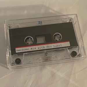 May include: A vintage cassette tape in a clear plastic case. The tape is dark gray with a red and white label that reads "Awesome Mix with Pro Label". The case is rectangular and transparent, showcasing the tape's details.
