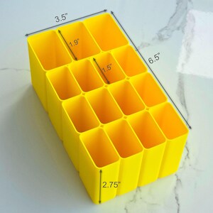 May include: A bright yellow organiser with 12 rectangular compartments. The organiser is 16.5 cm long, 8.9 cm wide, and 7 cm tall. Each compartment is 4.8 cm wide and 3.8 cm deep. Suitable for desk organisation.