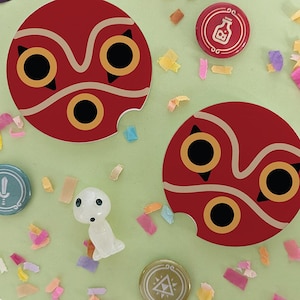 May include: Two red and white No Face mask stickers with a bite taken out of the bottom. The stickers are on a light green background with confetti.