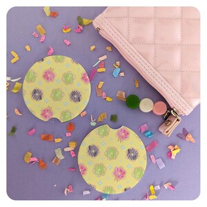 May include: Two yellow and green patterned coasters with a donut design. The coasters are on a purple surface with confetti.