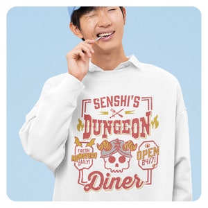 May include: White sweatshirt with a red and yellow graphic design that says "Senshi's Dungeon Diner" with a skull and crossbones logo. The text "Fresh Monsters Daily!" and "Open 24/7" are also included in the design.