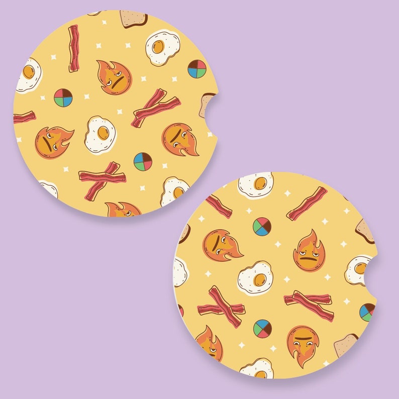 May include: Two round car coasters with a yellow background and a repeating pattern of fried eggs, bacon strips, toast, and flame-shaped faces. The coasters have a small notch for easy removal.