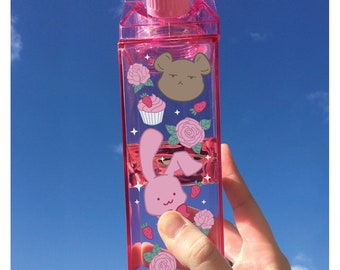 May include: Pink plastic milk carton shaped water bottle with a pink lid and various cartoon stickers including a bear, a bunny, a cupcake, and flowers.