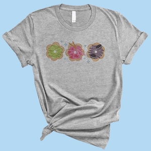 May include: A heather grey t-shirt with a design of three colorful donuts with different toppings.