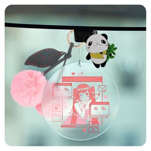 May include: A pink fuzzy ball charm, a green panda charm, and a clear round charm with a pink anime girl image on a car rearview mirror.