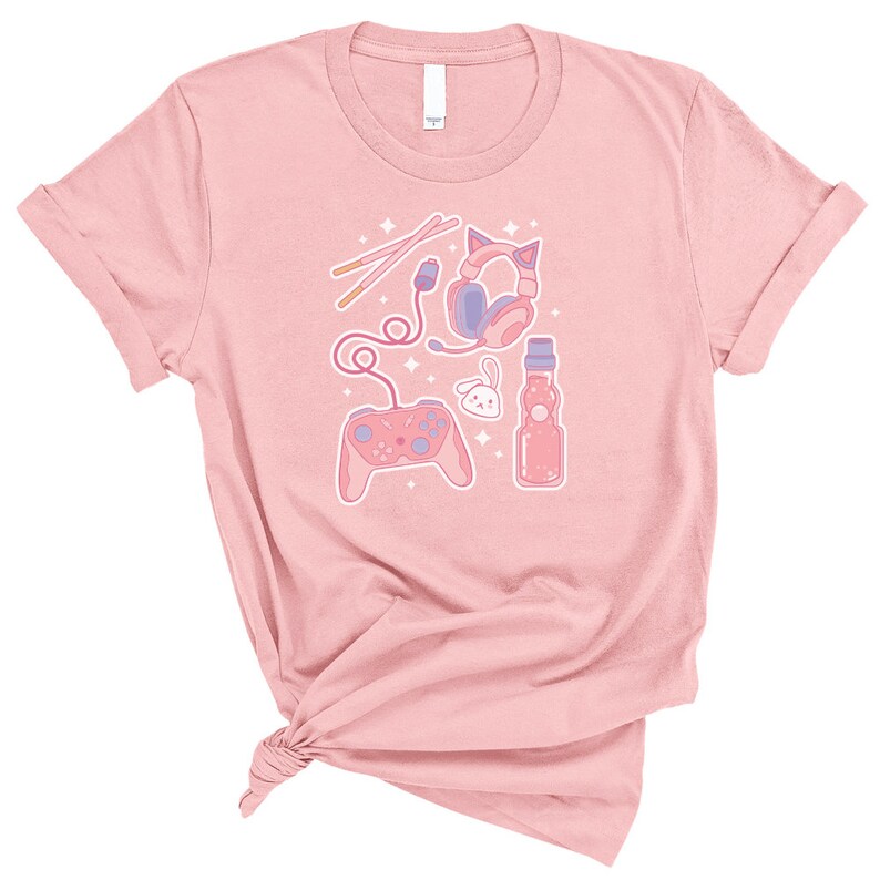K&ouml;nnte beinhalten: Pinkes T-Shirt mit einem Grafikdesign aus einem rosa und violetten Videospiel-Controller, Kopfh&ouml;rern, einer Flasche Ramune-Soda und einem rosa Hasen. Das Design ist von wei&szlig;en Sternen umgeben.