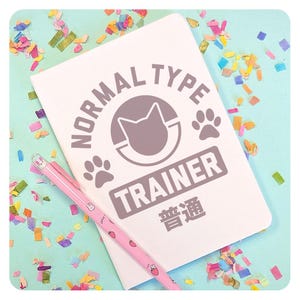May include: A white notebook with the text "NORMAL TYPE TRAINER" and a paw print graphic. The notebook is on a light blue background with confetti. The text "普通" is also on the notebook.
