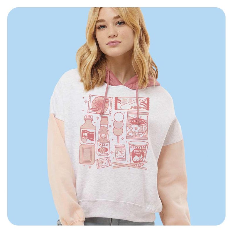 May include: A light gray hoodie with pink sleeves and a pink hood lining. The front of the hoodie features a pink graphic of Japanese snacks and drinks. The hoodie is made of a soft material.