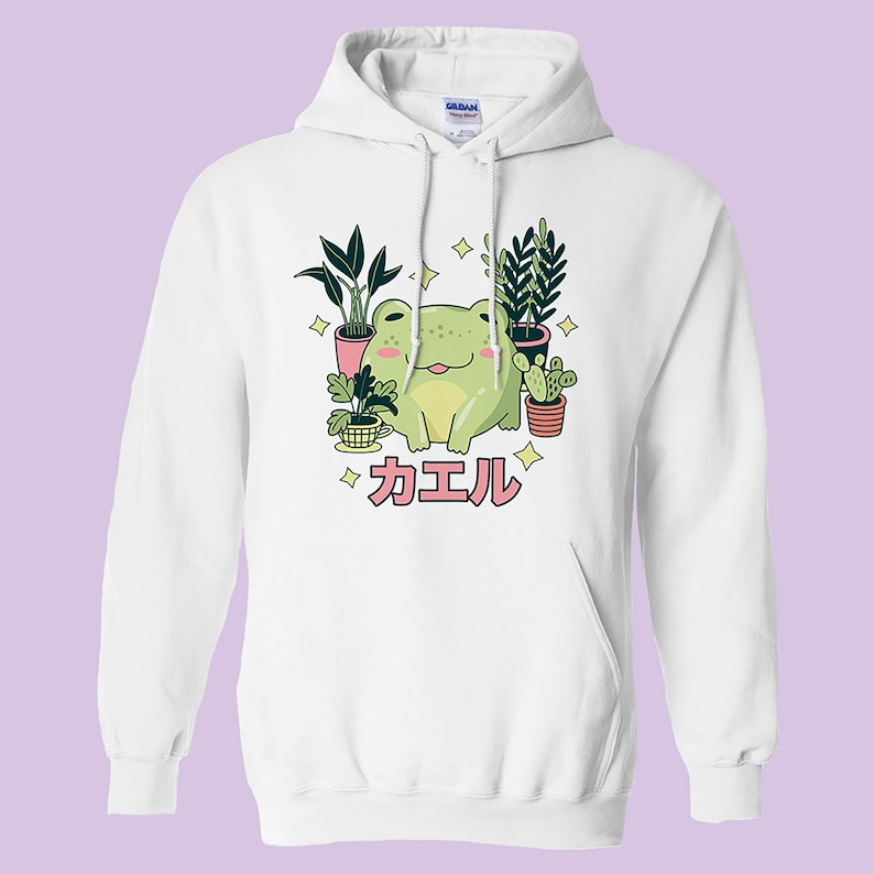 May include: White hoodie with a green frog sitting among potted plants. The frog is smiling and has a pink tongue sticking out. The text "カエル" is written in pink below the frog.