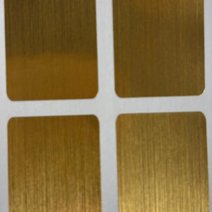 Op de afbeelding: Vier vierkante metalen platen met afgeronde hoeken en een geborstelde gouden afwerking. De platen zijn gerangschikt in een raster van twee bij twee, elk met verticale nerf. De goudkleur heeft een warme, metallic glans.