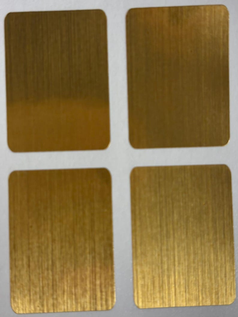 Op de afbeelding: Vier vierkante metalen platen met afgeronde hoeken en een geborstelde gouden afwerking. De platen zijn gerangschikt in een raster van twee bij twee, elk met verticale nerf. De goudkleur heeft een warme, metallic glans.