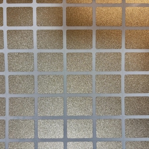 May include: Close-up of a sheet of gold glitter stickers. The stickers are rectangular with rounded corners and are arranged in a grid pattern. The background is white.