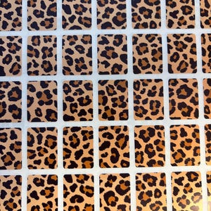 May include: A sheet of rectangular stickers with a leopard print pattern. The stickers have a tan background with brown and black spots. The stickers are arranged in a grid pattern on a white background.