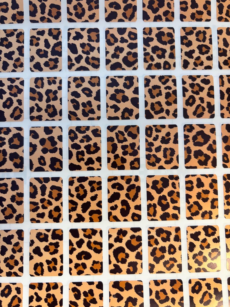 May include: A sheet of rectangular stickers with a leopard print pattern. The stickers have a tan background with brown and black spots. The stickers are arranged in a grid pattern on a white background.