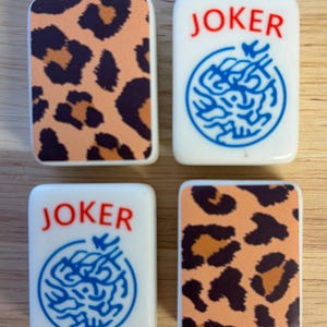 May include: Four rectangular Mahjong tiles. Two tiles feature a leopard print pattern in brown and orange. The other two tiles are white with the word "JOKER" in red and a blue circular design.
