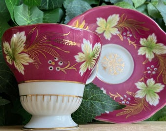 May include: A vintage teacup and saucer set. The cup and saucer are a deep magenta color with gold and white floral designs. The cup has a white base with gold trim, and the saucer has a matching design.