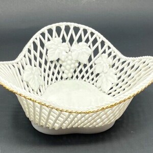 May include: White porcelain basket with a woven design and gold trim. The basket features a raised design of grapes and leaves.