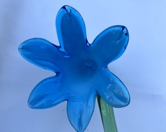 May include: A blue glass flower with five petals and a green stem. The flower is made of blown glass and has a delicate, whimsical design.