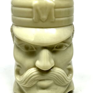 May include: A white plastic cup shaped like a man's head wearing a hat. The man has a moustache and a serious expression.