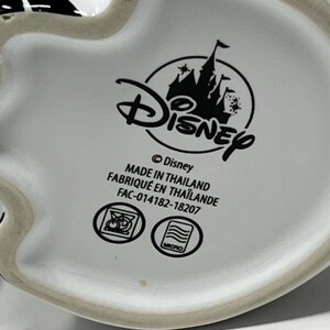 May include: White ceramic mug with a black and white Mickey Mouse design. The bottom of the mug features the Disney logo, text that reads "MADE IN THAILAND", and other symbols.