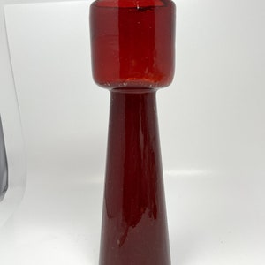 May include: A tall, red glass vase with a wide, cylindrical opening and a narrow, conical base.