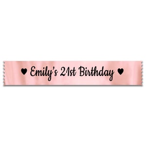 May include: Pink satin ribbon with black text that reads "Emily's 21st Birthday" with a black heart on each side.